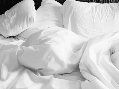 Helles Bett mit weißer Bettwäsche als Illustration zur Pflege von Wärmetextilien