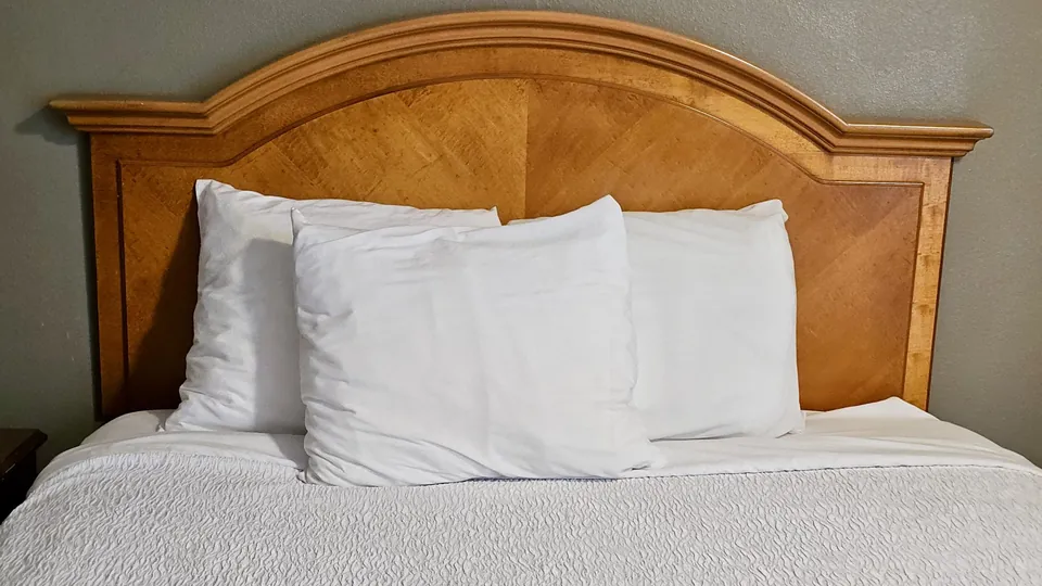 Bett mit weißer Bettwäsche und sichtbarem Holzrahmen
